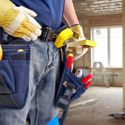 Handyman wearing a loaded tool belt and work gloves on a residential job site