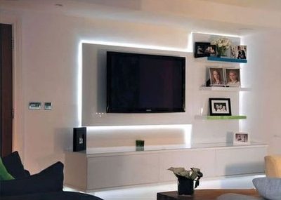 Wall-mounted TV recessed into a white built-in unit with LED cove lighting and display shelving